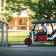 A side profile view of a battery-powered rickshaw as it drives through a park.